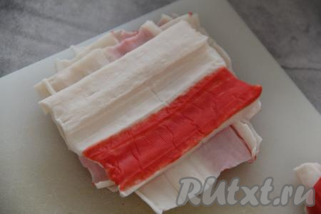 Каждую крабовую палочки аккуратно развернуть. Отрезать от развёрнутой крабовой палочки часть с красной полоской так, чтобы из крабовой палочки получился квадрат. Аналогично отрезать квадраты от всех крабовых палочек. Получившиеся квадраты отложить в сторону.