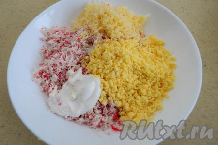 В тарелку с крабовыми палочками и желтками добавить сыр, натёртый на мелкой тёрке, сюда же выложить майонез, перемешать, немного подсолить (учитывая степень солёности сыра).