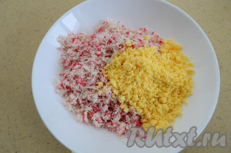 С крабовых палочек снять слюду. Натереть палочки на мелкой тёрке. Благодаря тому, что крабовые палочки не нарезаются, а натираются на тёрке, закуска получается особенно нежной. Сложить в глубокую тарелку крабовые палочки и 3/4 крошки из желтков.