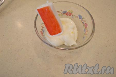 Желтки, которые мы откладывали ранее, переложить в тарелку и тщательно размять их вилкой. В пиалу выложить столовую ложку майонеза. Опустить половинку крабовой палочки одним концом в майонез.