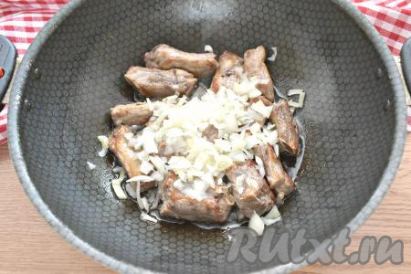 К обжаренным свиным рёбрышкам выкладываем лук, нарезанный на небольшие кусочки.