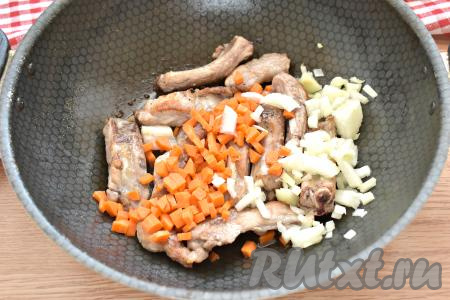 Очищаем морковку с луком. Лук нарезаем на небольшие кусочки, а морковку - на кубики (или брусочки). Добавляем лук и морковку к обжаренным рёбрышкам, перемешиваем. Убавляем огонь до среднего. Жарим, рёбра с овощами, иногда помешивая, 5 минут.