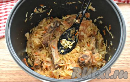 После завершения режима "Тушение" открываем мультиварку, добавляем к тушёной капусте и свиным рёбрам измельчённый зубчик чеснока, перемешиваем.