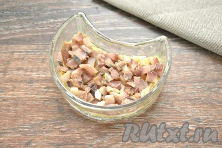 Филе сельди тщательно осматриваем, убирая косточки, после этого нарезаем на маленькие кубики и выкладываем равномерно поверх слоя картофеля.