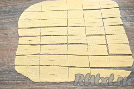 Раскатанный пласт нарезаем на полоски размером примерно 2 сантиметра на 5 сантиметров (можно чуть больше или меньше - не критично). В центре каждой полоски делаем надрез.