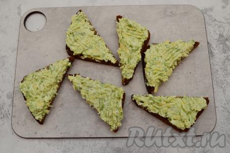 Кусочки чёрного хлеба разрезать на треугольники и смазать их подготовленной начинкой из авокадо, творожного сыра и белка.