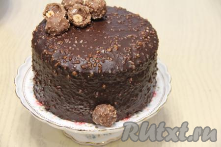 Приготовить ганаш - крем для украшения торта, для этого молоко и растительное масло нужно соединить в кастрюле и хорошо нагреть, снять с огня. В горячую смесь молока и растительного масла добавить кусочки шоколада и перемешать ганаш до полного растворения шоколада. Орехи измельчить в крошку и добавить в ганаш, перемешать. Снять бортики с торта и переложить его на решётку. Покрыть торт равномерно ганашем сверху и с боков, поставить в холодильник на 10 минут.