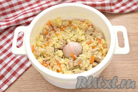 Достаём посуду из микроволновки, вода практически испарилась. Плов солим по вкусу, перемешиваем, в центр ставим целую промытую головку чеснока. Возвращаем кастрюлю в микроволновку, но уже без крышки.