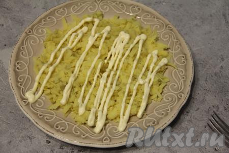 Почистить варёный картофель, натереть на крупной тёрке и равномерно выложить на плоскую тарелку. Натёртый картофель станет первым слоем нашего салата, нанести решётку из майонеза.