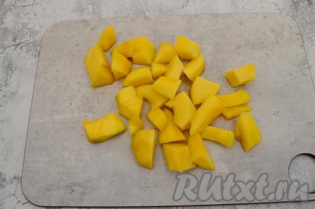 Затем разрезать пополам манго, вытащить косточку ложкой и очистить фрукт ножом от кожуры. Нарезать манго на крупные кубики.
