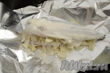 Подготовленную скумбрию посолить, смазать внутри и снаружи со всех сторон сметаной, а затем выложить рыбу поверх лука, лежащего на фольге. В брюшко скумбрии вложить оставшийся нарезанный лук.