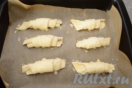 Сформированные рогалики ("язычком" вниз) выложить в форму для выпечки, застеленную пергаментом. Рогалики увеличатся в процессе выпечки, поэтому выкладывать их нужно на расстоянии друг от друга. Яйцо слегка взбить в небольшой ёмкости вилкой. Смазать рогалики сверху взбитым яйцом.&nbsp;Отправить выпекаться в разогретую до 200 градусов духовку на 20-25 минут. Рогалики должны увеличиться в размерах и подрумяниться.