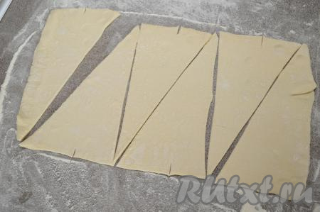 Острым ножом разрезать раскатанное тесто на треугольники, как на фото (у меня получилось 6 треугольников). В середине короткой стороны каждого треугольника сделать неглубокий надрез (глубиной примерно 1 сантиметр).