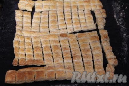 Размороженное тесто переложить на пергамент (или коврик для выпечки) и слегка раскатать. Затем нарезать на квадратики размером 1 сантиметр на 1 сантиметр. Поставить противень в разогретую духовку и выпекать слоёные квадратики минут 10-15 при температуре 200 градусов (до золотистого цвета). Затем квадратики из слоёного теста достать из духовки и полностью остудить.