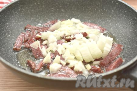 К обжаренной колбасе выкладываем достаточно мелко нарезанный лук, перемешиваем, обжариваем 2-3 минуты, не забывая иногда помешивать.