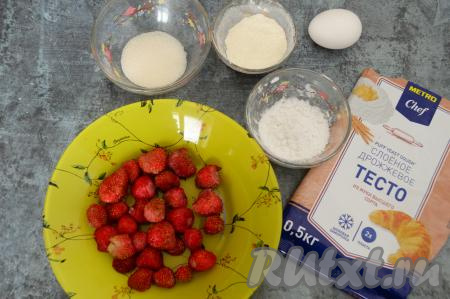 Подготовить продукты для приготовления слоек с замороженной клубникой. Клубнику достать из морозилки, оставить при комнатной температуре минут на 10, затем лишнюю воду слить. Ягоды не нужно полностью размораживать. Слоёное тесто подойдёт и дрожжевое, и бездрожжевое, достать его из морозилки заранее, чтобы оно разморозилось при комнатной температуре.