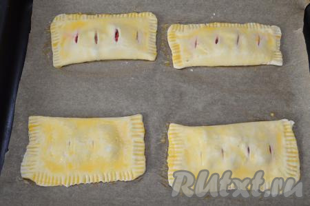 Сформировать таким образом все 4 слойки с замороженной клубникой, переложить их на противень, застеленный пергаментом. В небольшой ёмкости взбить вилкой сырое яйцо. С помощью силиконовой кисточки смазать поверхность слоек яйцом.