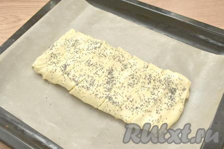 На противень, застеленный ковриком для выпечки (или пергаментной бумагой), перекладываем сформированный слоёный пирог. В небольшой ёмкости взбиваем вилкой яйцо. Смазываем пирог с помощью кулинарной кисти взбитым яйцом. По желанию, верх пирога посыпаем маком (или кунжутом).