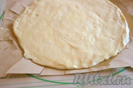 "Отдохнувшее" тесто достать из холодильника и разделить на две части. Раскатать каждую часть теста на присыпанной мукой поверхности в пласт диаметром примерно 28 сантиметров и толщиной 1 сантиметр. Первую часть раскатанного теста выложить в форму для выпечки, формируя небольшие бортики. Я раскатанное тесто переложила вначале на бумагу для выпечки, а уже затем поместила в форму для выпечки, формируя бортики. При желании, можно готовить и без бумаги, слегка смазав форму маслом.