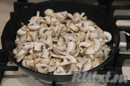 Обжарить лук с курицей в течение 10 минут, иногда перемешивая. Шампиньоны нарезать на пластинки и тоже добавить в сковороду.