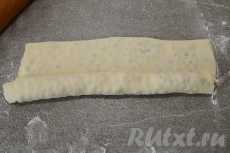 Затем, начиная с длинного края, свернуть тесто с изюмом в рулет.