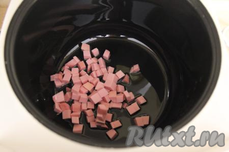 В чашу мультиварки влить масло и выставить режим "Жарка". Колбасу нарезать на средние кубики и выложить в чашу.