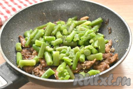 После того как свинина обжарится с кунжутом 1 минуту, добавляем в сковороду фасоль, немного солим (помним, что мы тушили мясо в соевом соусе, а он уже солёный).