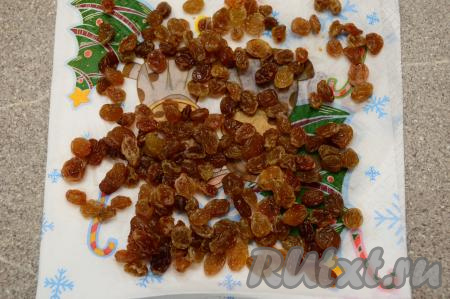 Изюм промыть тёплой водой, переложить в глубокую тарелку, полностью залить кипятком и оставить минут на 5, затем откинуть на сито, чтобы стекла лишняя вода, после этого выложить ровным слоем на бумажную салфетку и дать немного обсохнуть.