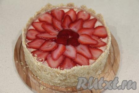 После того как творожная основа застынет, займёмся заливкой. В небольшой ёмкости 7 грамм желатина и 1 чайную ложку сахара залить 100 миллилитрами холодной воды, тщательно перемешать и оставить желатин набухать минут на 15. Прогреть набухшую желатиновую смесь, не переставая помешивать, до полного растворения кристаллов желатина. Клубнику для чизкейка можно взять свежую или замороженную. Я использовала замороженную клубнику, предварительно её немного разморозила. Если готовите со свежей клубникой, тогда её нужно промыть водой, убирая чашелистики, а после этого обсушить. Ягоды нарезать на пластинки (или на мелкие кубики). Выложить клубнику поверх застывшей творожной основы. Немного остудить желатиновую массу, а затем аккуратно влить её поверх клубники. Поставить чизкейк на час в холодильник (до полного застывания заливки).