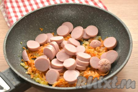 Сосиски нарезаем на кружочки толщиной 5-7 миллиметров и добавляем к обжаренным овощам, перемешиваем. Обжариваем сосиски с морковкой и луком 2-3 минуты, время от времени помешивая.