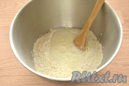 В центр смеси из сухих ингредиентов вливаем молоко, заранее подогретое до 38-40 градусов, и оливковое (или подсолнечное) масло, перемешиваем вначале лопаткой (или ложкой).
