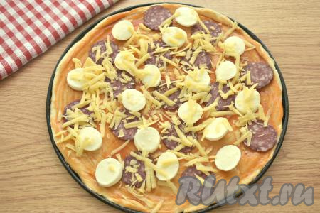 Сыр твёрдых сортов натираем на крупной тёрке. Посыпаем пиццу сверху половиной натёртого сыра.