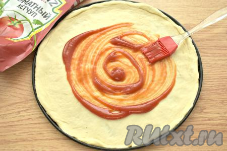 Тесто делим на 2 части (будем готовить 2 пиццы). Вначале на присыпанной мукой поверхности раскатываем одну часть теста в круг диаметром 25 сантиметров. Форму для выпечки (или противень) смазываем растительным маслом (или застилаем пергаментом), выкладываем раскатанное тесто, формируя небольшие бортики, и смазываем его 1-1,5 столовыми ложками кетчупа.