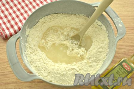 Воду подогреваем до 36-37 градусов и вливаем в центр смеси муки и дрожжей, добавляем оливковое (или подсолнечное) масло, перемешиваем тесто вначале ложкой, а затем тщательное вымешиваем его руками.