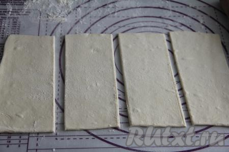 Пласт слоёного теста на присыпанной мукой поверхности слегка раскатать скалкой и разрезать на 4 прямоугольника.