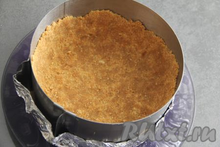 Получившуюся массу выложить в форму для выпечки диаметром 18 сантиметров (я взяла кулинарное кольцо и сформировала дно из фольги, сложенной в несколько слоёв). Сформировать из печенья с маслом основу чизкейка, тщательно утрамбовывая дно и формируя высокий бортик. Убрать форму с основой в холодильник на время, пока будем заниматься творожной начинкой чизкейка.