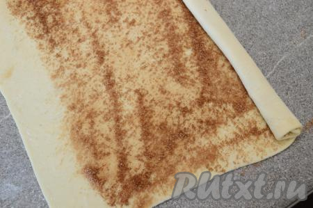 Начиная с длинного края, посыпанного корицей, скрутить пласт теста в рулет.