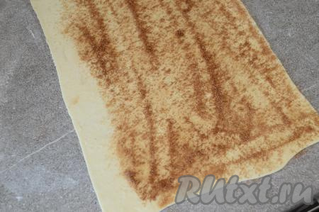 На раскатанный пласт слоёного теста равномерно нанести смесь сахара и корицы, отступив 2 сантиметра от одного длинного края теста, как на фото.