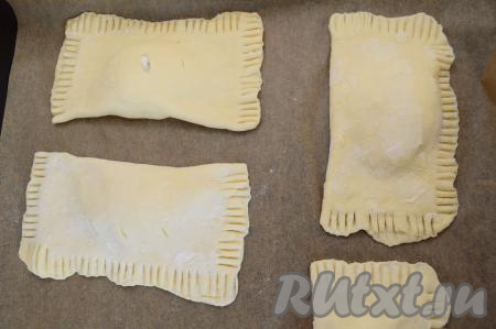 Выложить заготовки слоек с творогом и бананом на противень, застеленный бумагой для выпечки. Яйцо в небольшой ёмкости взбить вилкой до однородности. Сверху смазать каждую слоечку взбитым яйцом.