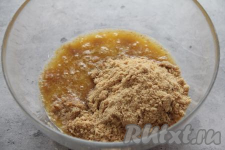 Сливочное масло растопить, влить в миску, добавить крошку из печенья, перемешать массу столовой ложкой до однородности.