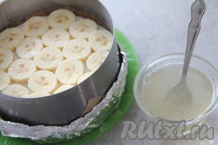 Когда начинка застынет, можно заняться заливкой. Желатин нужно соединить с сахаром и водой, перемешать и дать набухнуть в течение минут 10, затем прогреть, помешивая, на среднем огне до полного растворения желатина (очень важно, чтобы желатин растворился, но при этом не был доведён до кипения).&nbsp;Дать желатиновой смеси немного остыть. 2 банана очистить, нарезать на кусочки толщиной примерно 1-1,5 сантиметра и выложить поверх застывшего творожного слоя чизкейка.