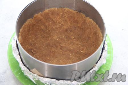 Получившуюся песочно-масляную массу выложить в разъёмную форму, утрамбовать дно и сформировать высокий бортик, у нас получится основа чизкейка. Я в качестве формы взяла кулинарное кольцо диаметром 18 сантиметров без дна. Дно формы я сделала из пергамента и фольги, сложенной в два слоя, а затем поставила подготовленную форму на плоское блюдо и сформировала из песочно-масляной массы основу чизкейка. Форму с основой чизкейка поставить в холодильник на время, пока будем готовить творожную начинку.