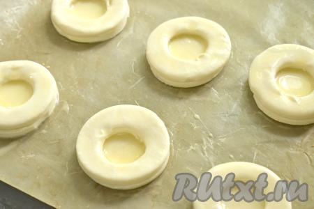 На противень, застеленный ковриком (или бумагой) для выпечки выкладываем целые кружки на расстоянии друг от друга, смазываем взбитым яйцом. Сверху помещаем кружки с отверстиями, тоже смазываем яйцом, захватывая бока. Заготовки волованов из слоёного теста отправляем в разогретую до 190 градусов духовку на 15-20 минут (до подрумянивания выпечки).