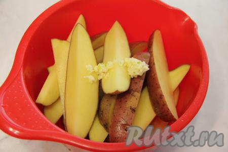 Клубни картофеля лучше взять одного размера, тогда время запекания будет одинаковым. Картошку по-деревенски можно готовить в кожуре (если у вас клубни с тонкой шкуркой), тогда тщательно вымойте картошины, счищая всю грязь железной щёткой. Можно, конечно, картофель и очистить от кожуры. Нарезать подготовленную картошку на крупные дольки. Чеснок почистить и пропустить через пресс. Добавить чеснок в миску с картошкой.