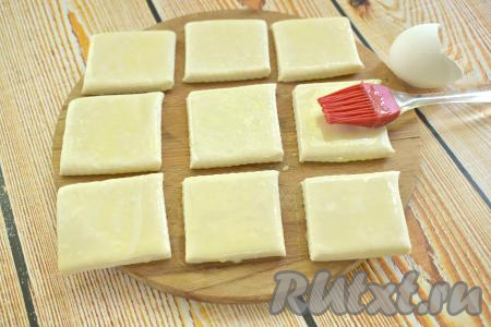 В небольшой ёмкости взбиваем вилкой яйцо. Квадратики из слоёного теста смазываем взбитым яйцом.