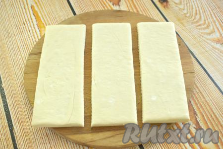 Размороженный пласт теста кладём на стол (раскатывать его не нужно), разрезаем на 3 равных полоски (у меня полоски шириной 6 сантиметров и длиной 18 сантиметров).