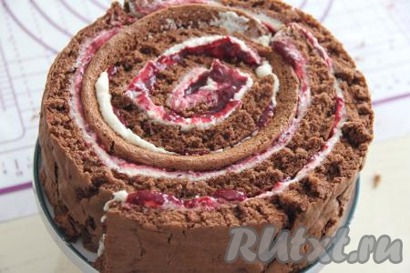 Разрезать корж по длине на 4 полоски равной ширины. Вначале одну полоску свернуть в достаточно плотный рулетик, а затем остальные полоски аккуратно обернуть вокруг рулетика, формируя в виде спирали торт с крем-чизом и начинкой из вишни.