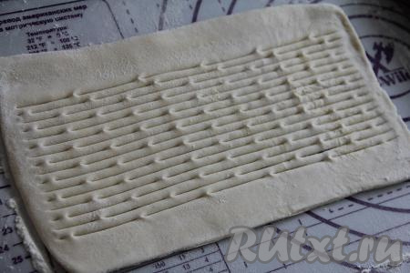 Второй пласт теста тоже слегка раскатать, затем сделать на нём фигурным ножом надрезы (если фигурного ножа нет, можно нарезать тесто на полоски и выложить на начинку). Надрезы на поверхности пирога нужны для того, чтобы через них в процессе выпечки из начинки выходил пар.