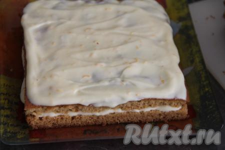 Корж выровнять, отрезав края по периметру. Обрезки не выбрасываем, их будем использовать для посыпки готового медовика. Корж разрезать на 4 квадрата, а затем разрезать каждый квадрат на две части, у нас получатся 8 коржей. Собрать медовик, обильно смазывая каждый корж апельсиновым кремом и складывая коржи один на другой. Верх и бока медовика тоже смазать кремом.