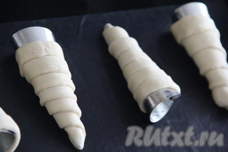 Трубочки можно сформировать с помощью металлических конусов, которые можно купить в магазине для кондитеров. Если таких конусов нет, тогда можно сформировать конусы из пищевой фольги. Конусы смазать растительным маслом и обмотать полосками теста. Полосочки должны плотно прилегать друг к другу, не внахлёст. Переложить заготовки слоёных трубочек на противень, застеленный ковриком для выпечки (или пекарской бумагой).